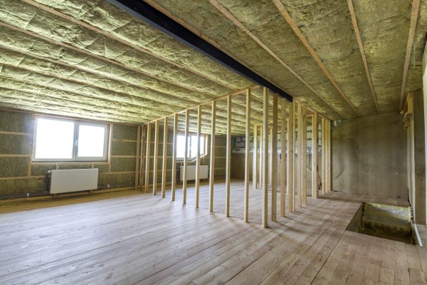 Construction and renovation of big light spacious empty room with oak floor, walls and ceiling insulated with rock wool, heating radiators under low attic windows and wooden frame for future walls.