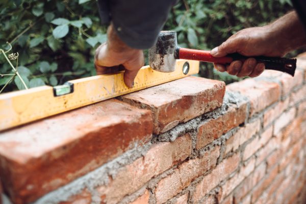 professional construction worker laying bricks and building brick walls in industrial site. Detail of hand adjusting bricks